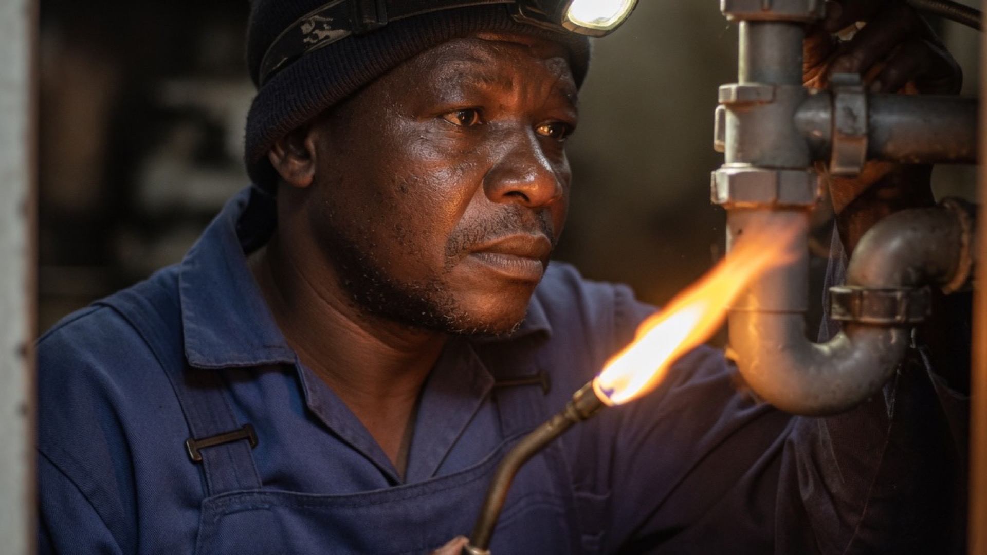 A Du Toit plumber in navy overalls with a headlamp
